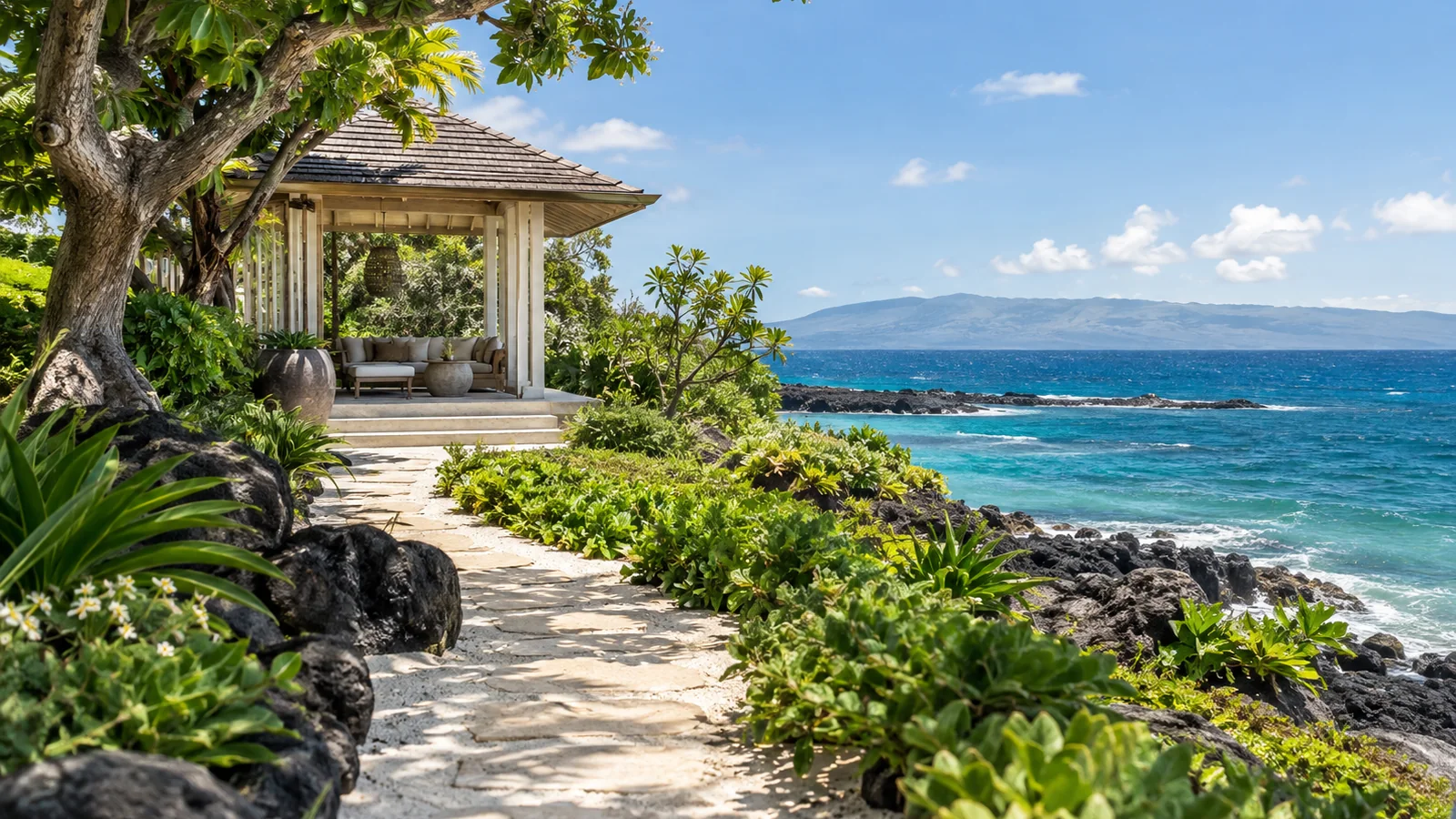 A pale coastal path through tropical greenery to an open pavilion beside the Hawaiian ocean